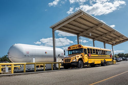 A school bus sitting under a large shelter area next to a propane tank