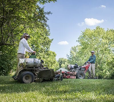 Two members of the Greenwood Group mowing a lawn with propane lawnmowers