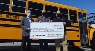 Three men hold a giant check in front of a school bus