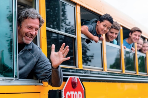 A smiling school bus driver and kids waving