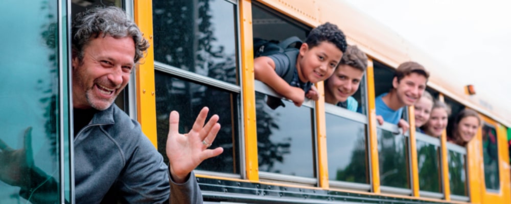 A smiling school bus driver and kids waving
