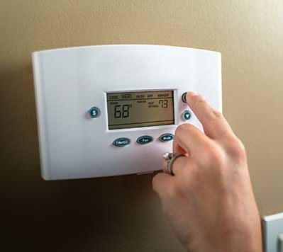 A woman's hand adjusting a home thermostat