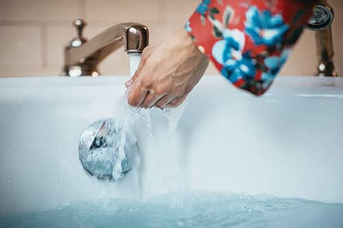 A women testing the temperature of running water from the bath tub faucet