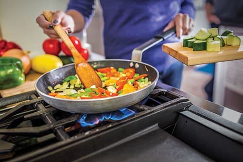 Woman sauteeing bell peppers in a pan on a propane kitchen range