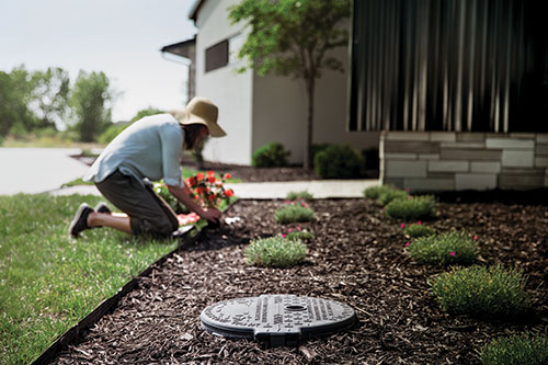 A woman gardening in a flower bed with an access point to an underground propane tank